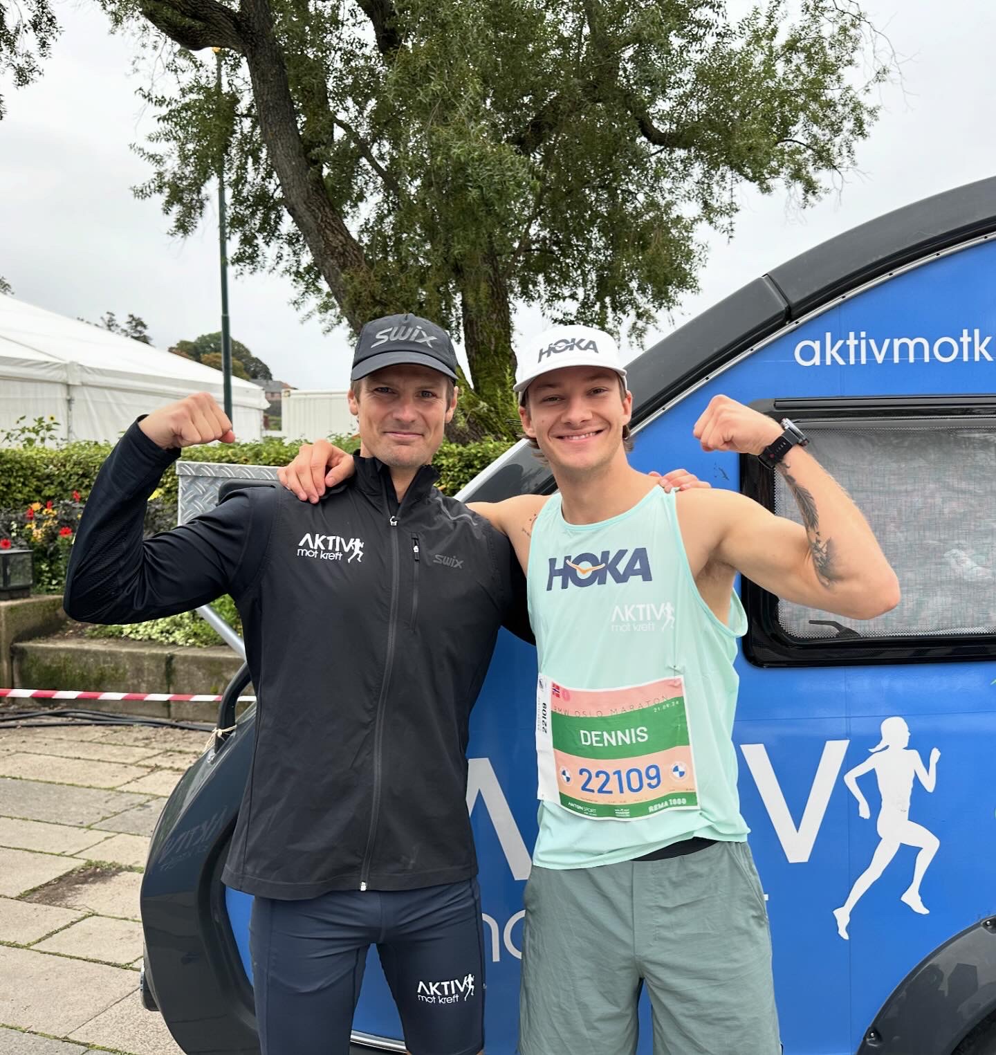 To people posing outdoors in athletic gear, flexing their muscles, in front of a promotional vehicle for Aktiv mot kreft.