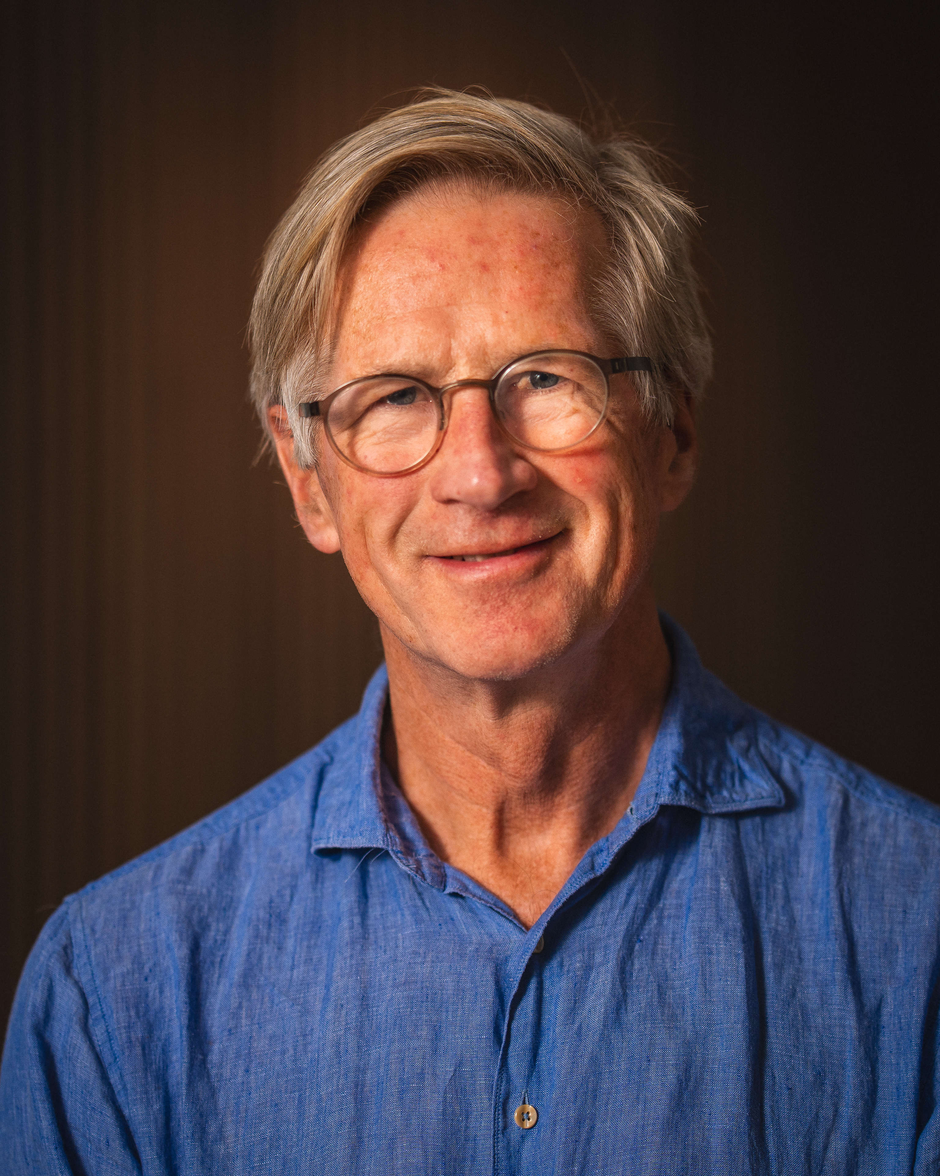 Portrett av en mann med briller og lys blå skjorte, smilende mot kamera.