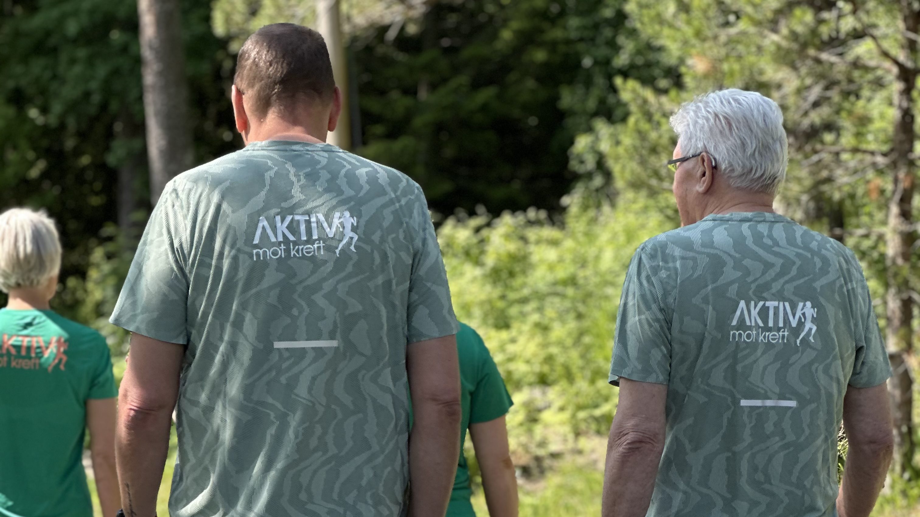 To menn iført matchende sportsklær går sammen på en grusvei, omgitt av grønn vegetasjon.